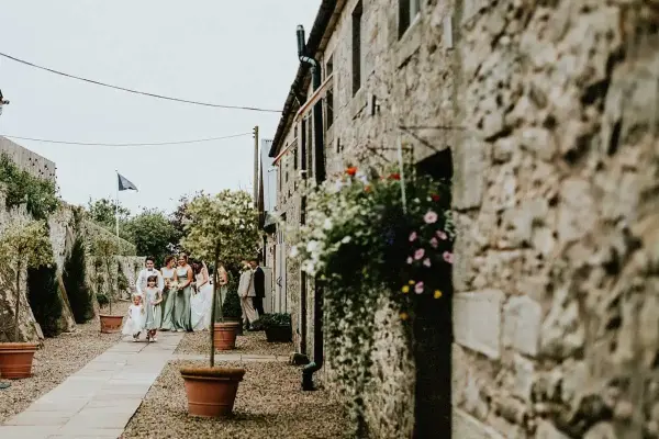 Charming outdoor pathway lined with rustic stone walls, potted plants, and blooming flowers, creating a romantic ambiance for ceremonies.