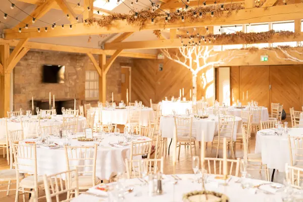 Charming rustic venue featuring wooden beams, elegantly set round tables, and soft lighting, ideal for a cozy wedding reception.