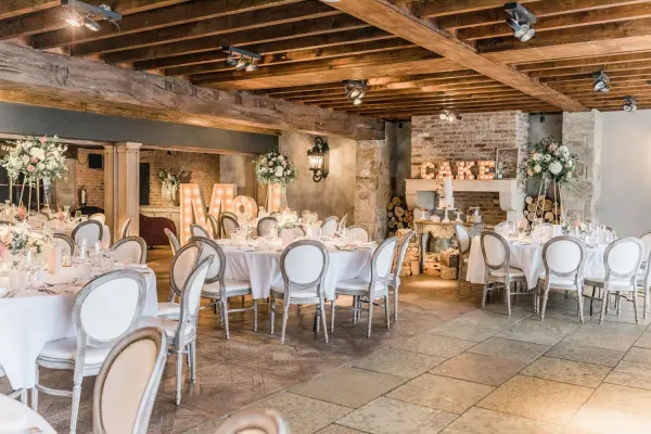Charming indoor wedding venue with rustic wood beams, elegantly set tables, and warm lighting, perfect for intimate receptions.