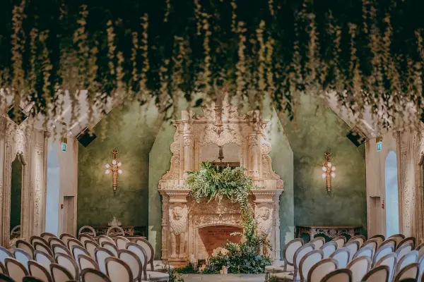 Charming indoor ceremony space featuring a lush floral backdrop, elegant seating, and a beautifully designed fireplace.