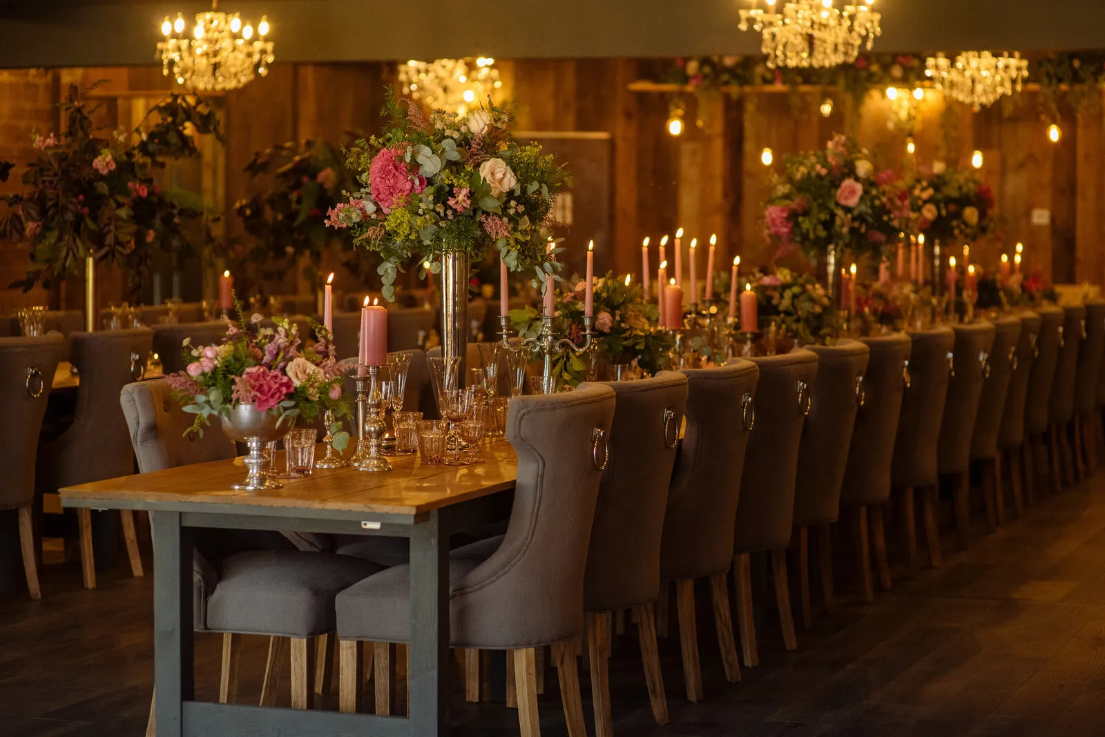 Elegant reception hall featuring long wooden tables adorned with lush floral centerpieces and soft candlelight, perfect for intimate gatherings.