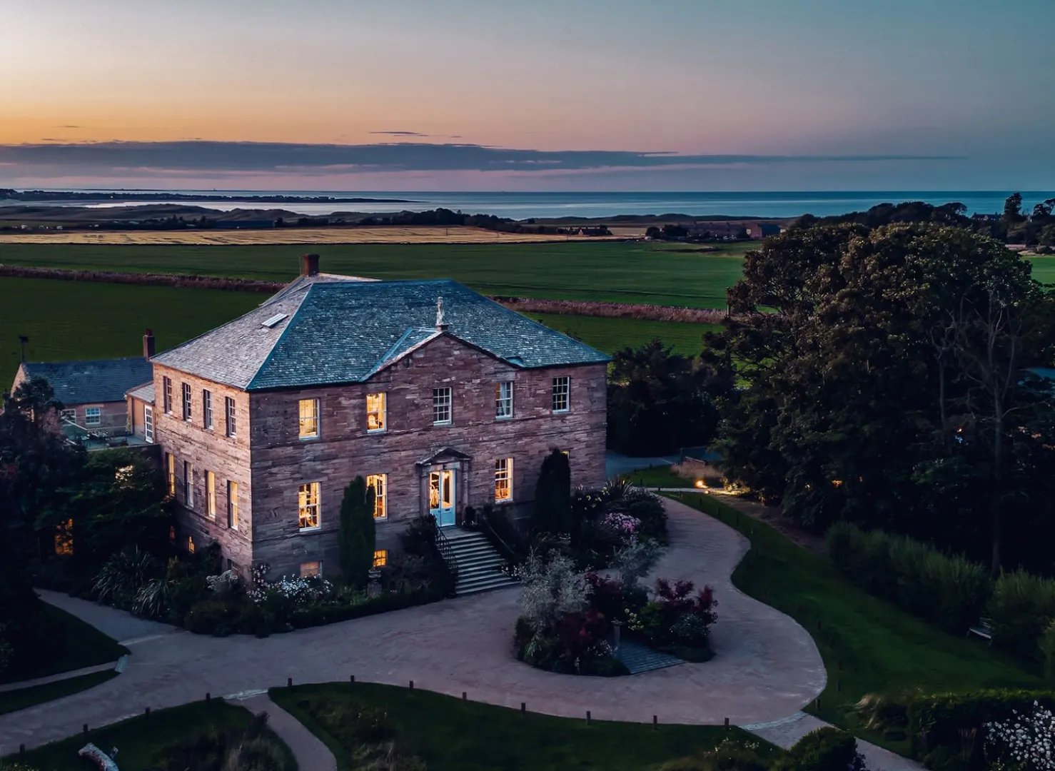 Stunning sunset view of a historic stone house, surrounded by lush greenery and open fields, perfect for elegant outdoor ceremonies.