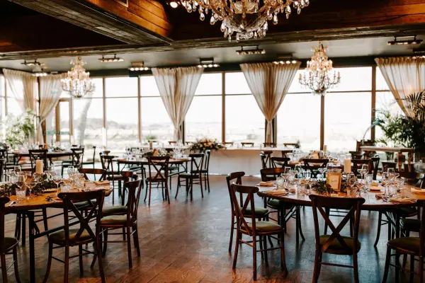 Bright and airy reception space featuring elegant chandeliers, wooden tables, and large windows with scenic views, perfect for a romantic wedding.