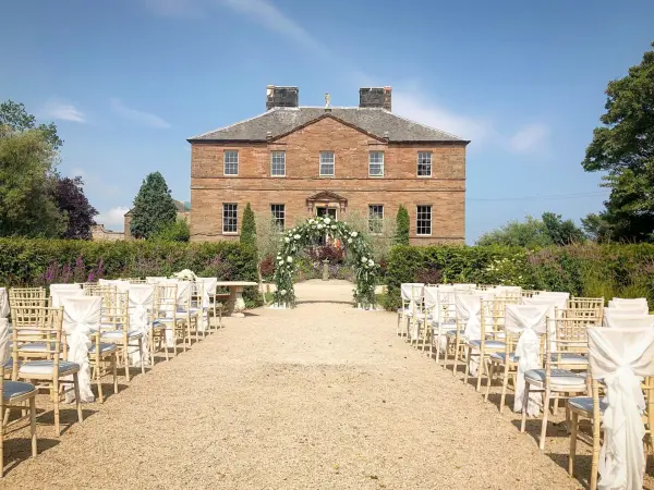 Charming outdoor ceremony space lined with decorated chairs, leading to a historic stone building surrounded by lush greenery.