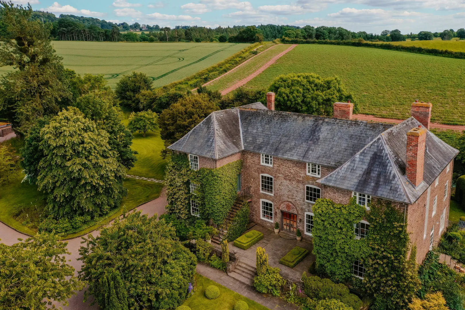 Elegant countryside venue featuring a charming historic home, surrounded by lush greenery and open fields, perfect for outdoor ceremonies.