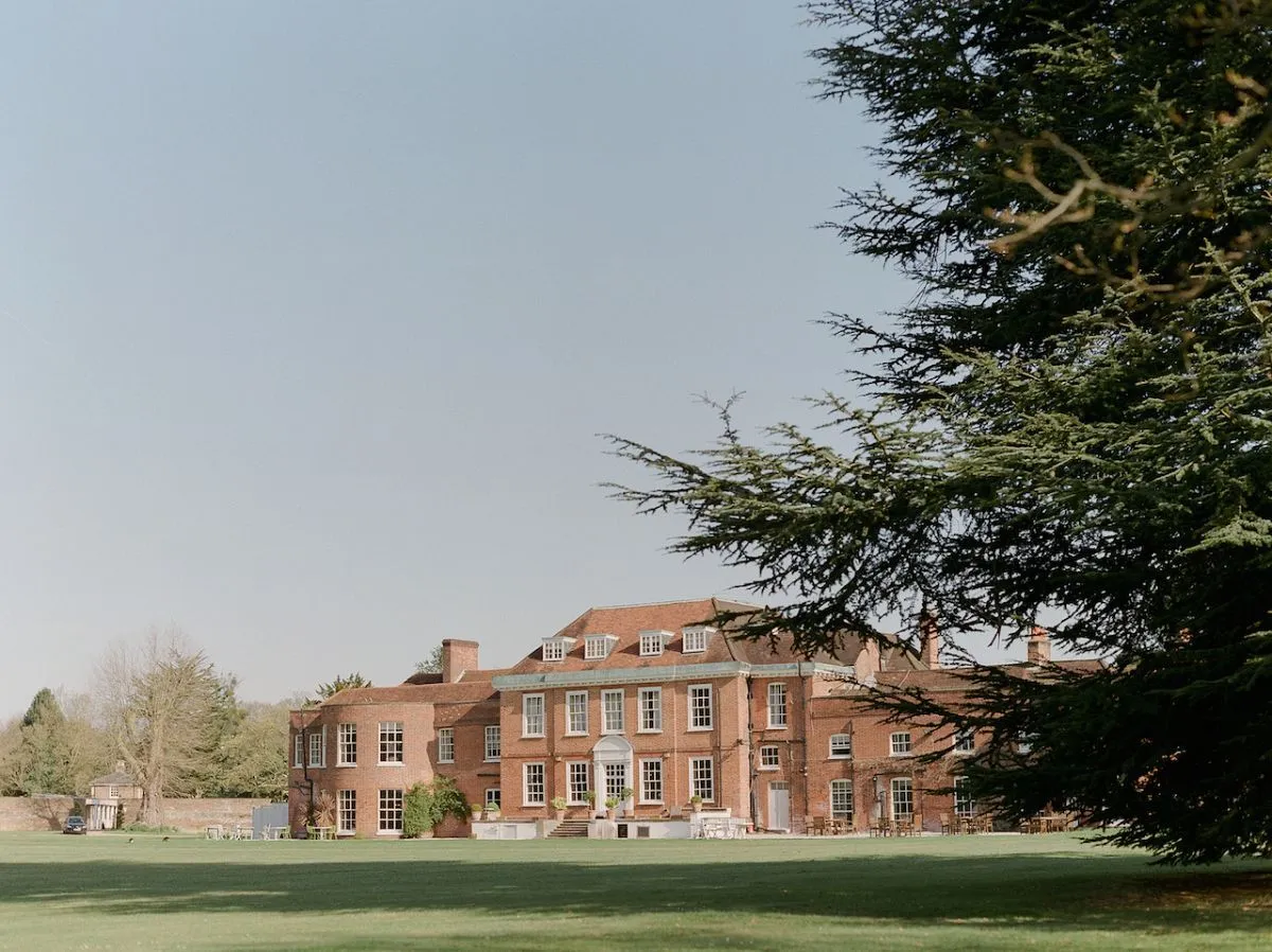 Stunning historic mansion with sprawling green lawns, framed by tall trees, perfect for elegant outdoor ceremonies and receptions.