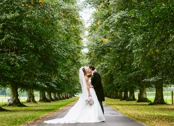 A romantic couple kisses in an enchanting tree-lined avenue, creating a serene and intimate wedding backdrop.