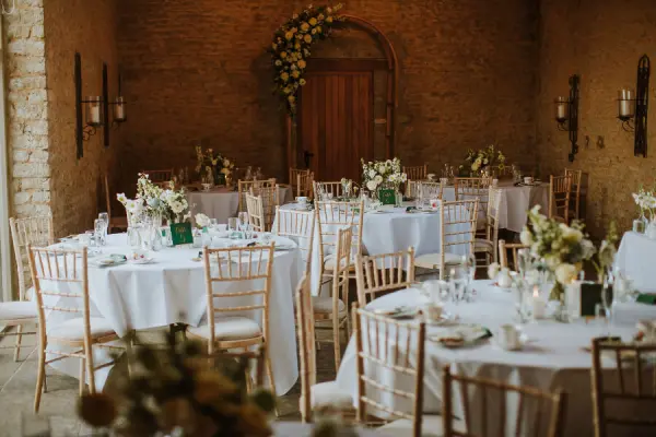 Charming reception area featuring elegantly set tables, rustic stone walls, and lush floral arrangements, perfect for intimate celebrations.