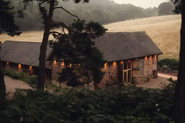 Charming rustic barn surrounded by lush greenery and golden fields, perfect for intimate wedding celebrations. Soft lighting enhances its warmth.