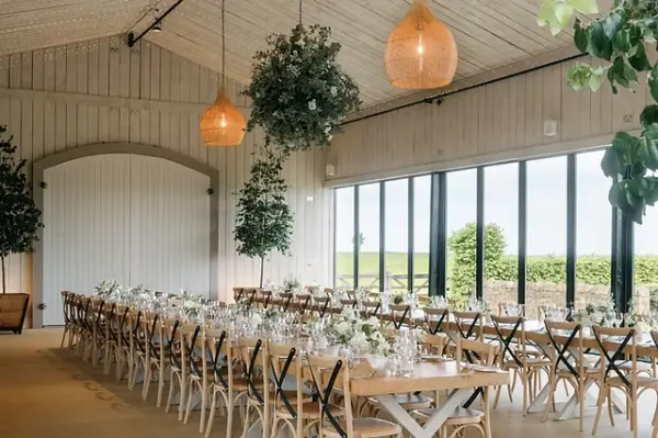 Bright, airy reception space featuring long wooden tables, lush floral arrangements, and large windows with scenic views.