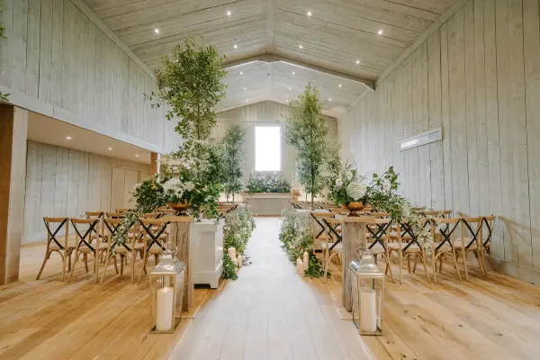 Elegant wooden venue featuring rows of rustic chairs, greenery decor, and soft lighting, ideal for a romantic wedding ceremony.
