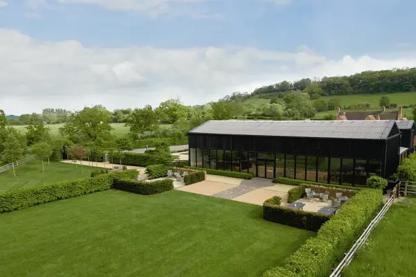 Modern barn venue with expansive glass walls, surrounded by lush greenery and manicured gardens, ideal for a scenic outdoor ceremony.
