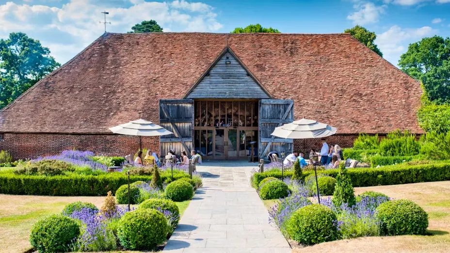Charming rustic barn venue surrounded by manicured gardens, outdoor seating, and vibrant lavender in a serene countryside setting.