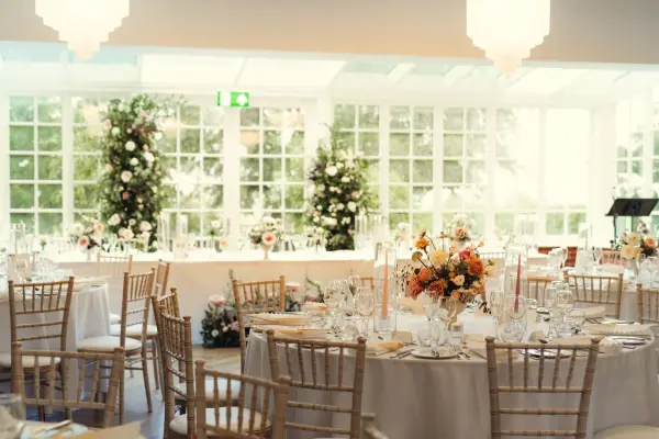 Bright, modern reception space featuring elegantly set tables, lush floral arrangements, and large glass windows for natural light.