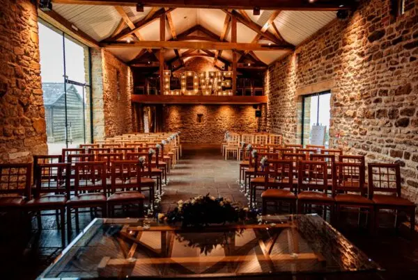 Stylish rustic barn interior featuring rows of wooden chairs, exposed stone walls, and a "LOVE" light display for an intimate wedding setting.