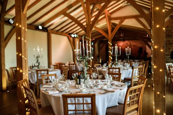 Charming rustic barn with exposed wooden beams, elegantly set tables, and soft lighting, perfect for an intimate wedding reception.