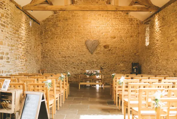Rustic ceremony space featuring exposed stone walls, wooden beams, and wooden chairs adorned with floral accents for an intimate wedding setting.