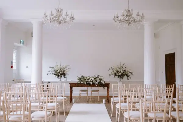 Bright reception space featuring elegant white walls, crystal chandeliers, and rows of chiavari chairs, perfect for intimate ceremonies.