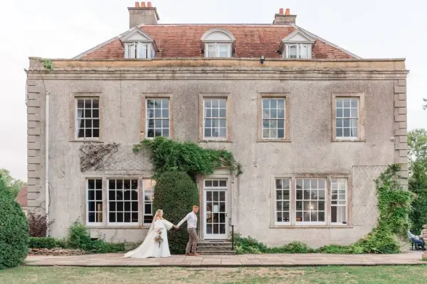 Charming historic facade featuring a couple in front of an elegant, weathered estate with lush greenery and large windows. Perfect for outdoor ceremonies.