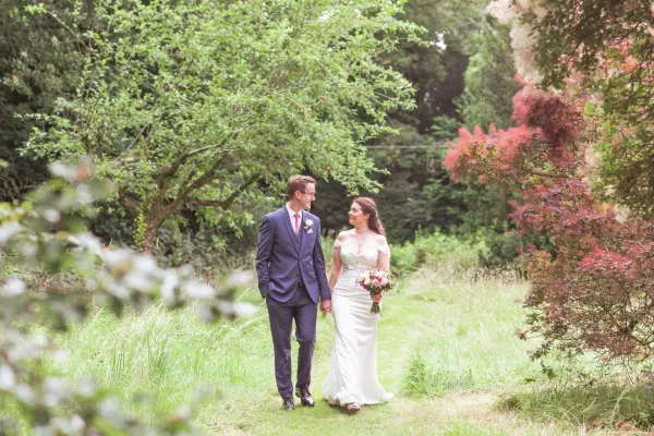 A couple strolls hand in hand through a lush garden path, surrounded by vibrant greenery and blooming trees, ideal for romantic outdoor ceremonies.