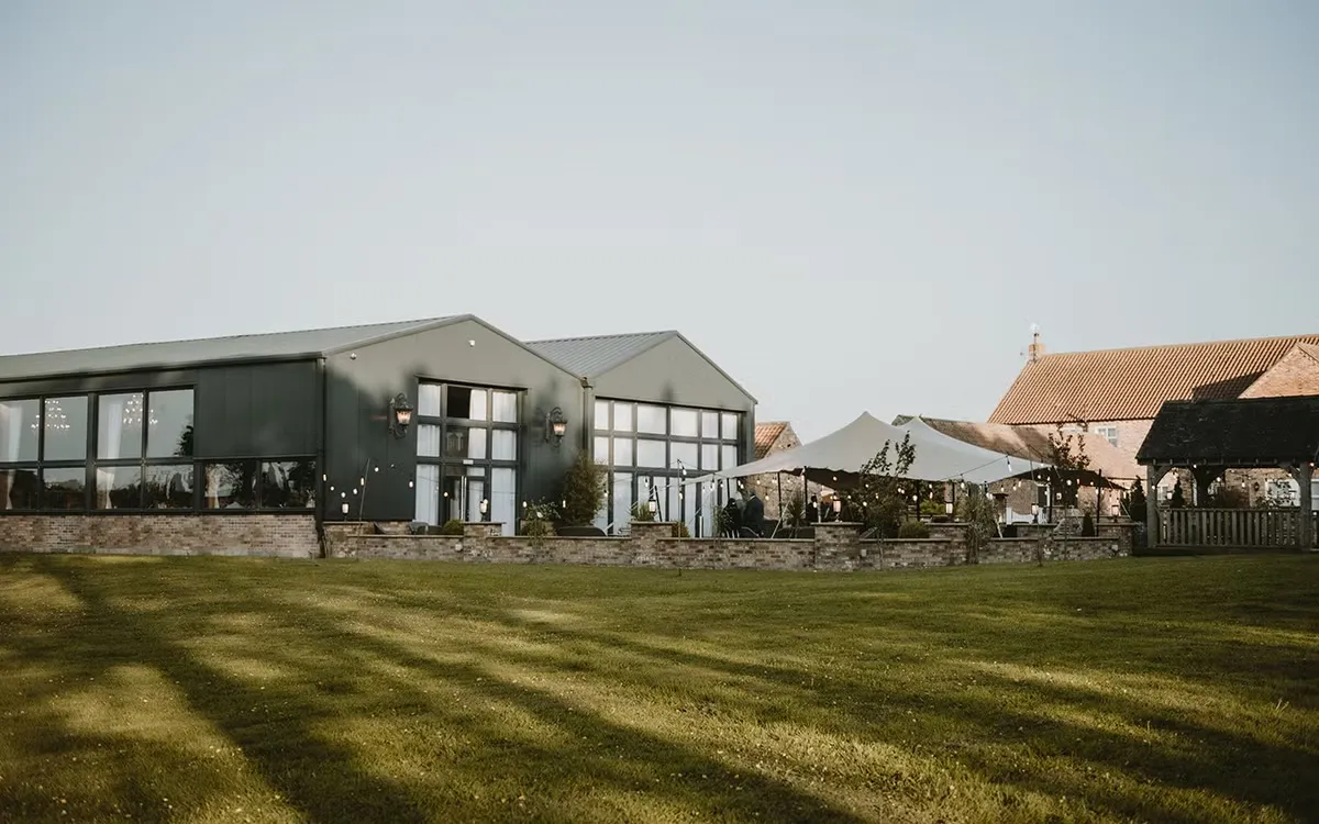 Spacious wedding venue featuring modern buildings, lush green lawns, and a stylish outdoor ceremony space with a charming tent.