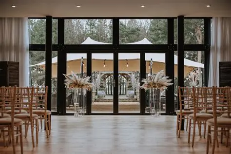 Elegant indoor ceremony space with wooden chairs, leading to a charming outdoor tented area surrounded by lush greenery.