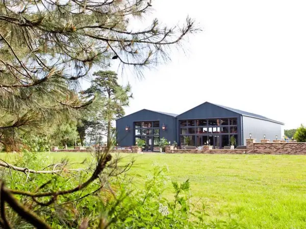 Charming barn-style venue surrounded by lush greenery, featuring large windows and an inviting outdoor space for ceremonies or receptions.