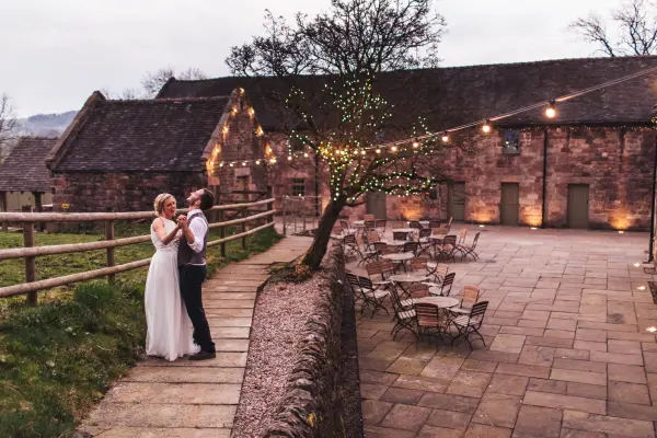 Couple dancing on a stone pathway, surrounded by rustic stone buildings and twinkling lights in a charming outdoor space.