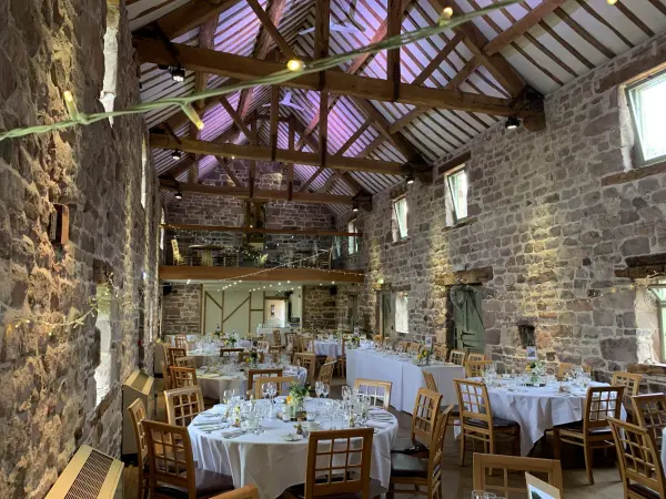 Rustic barn venue featuring exposed stone walls, wooden beams, and elegantly arranged round tables for a charming wedding reception.