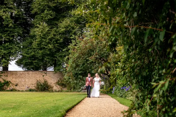 A serene garden pathway lined with trees, featuring a bride and groom walking together, ideal for romantic outdoor ceremonies.