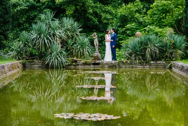 A serene pond surrounded by lush greenery and elegant statues, ideal for intimate outdoor wedding photos.