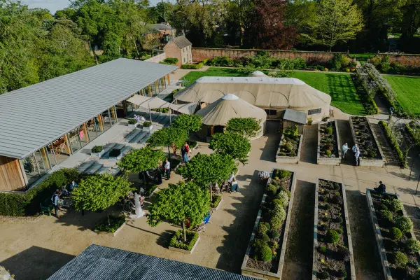 Charming outdoor wedding venue with lush gardens, elegant tent structures, and a modern reception space surrounded by greenery.