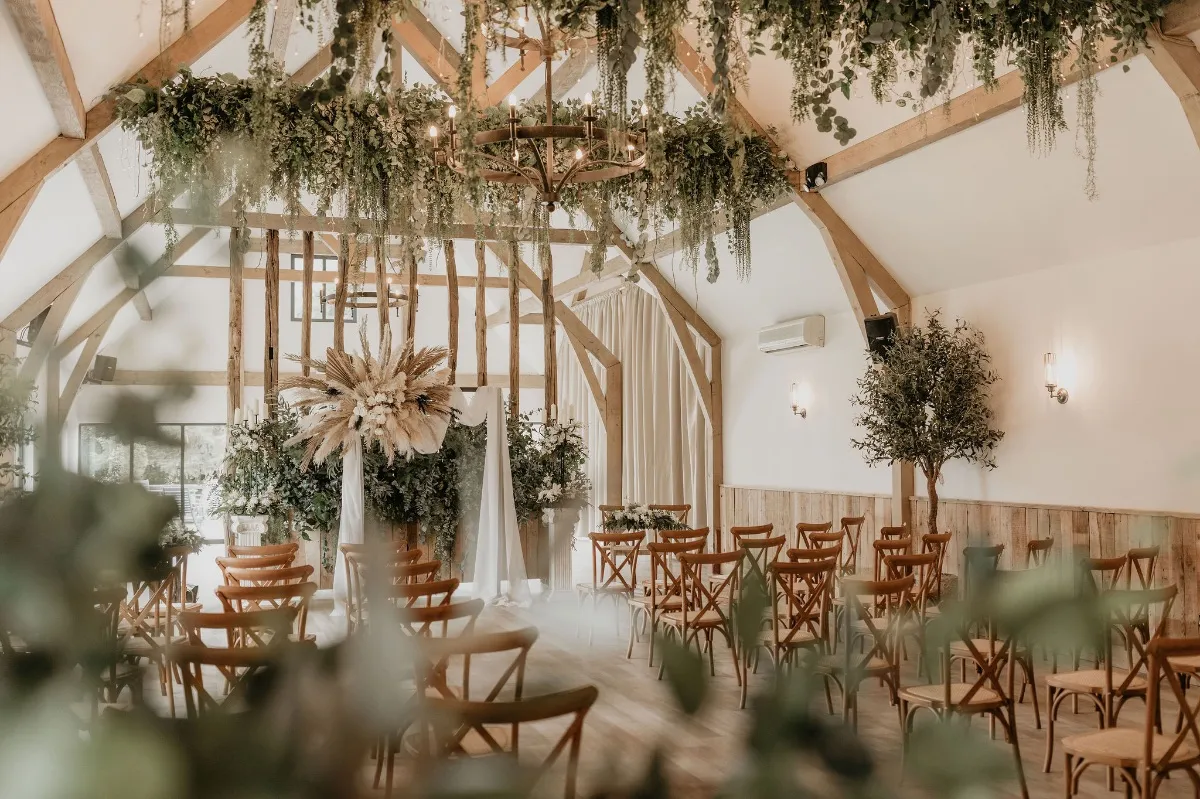 Rustic indoor venue featuring wooden beams, greenery accents, and elegant seating arranged for a romantic ceremony.