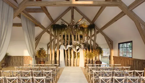 Rustic ceremony space featuring wooden beams, natural decor, white drapery, and elegant seating, perfect for intimate weddings.