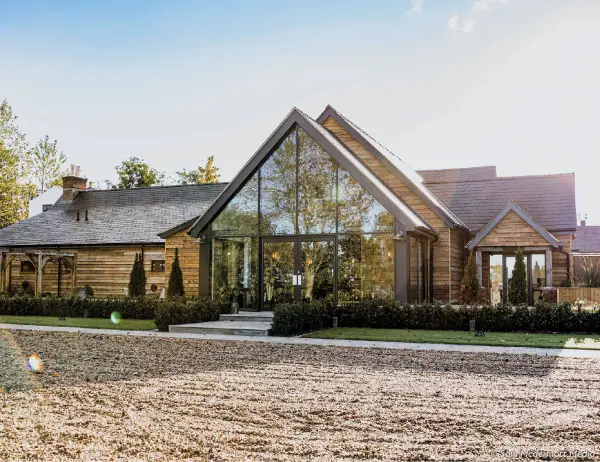 Charming rustic venue featuring a modern glass entrance, surrounded by manicured greenery and a gravel approach, perfect for intimate weddings.