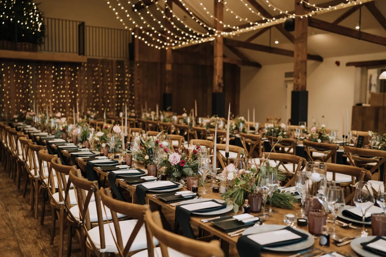 Rustic wooden tables adorned with elegant centerpieces, candlelight, and string lights create a warm, inviting atmosphere for a wedding reception.