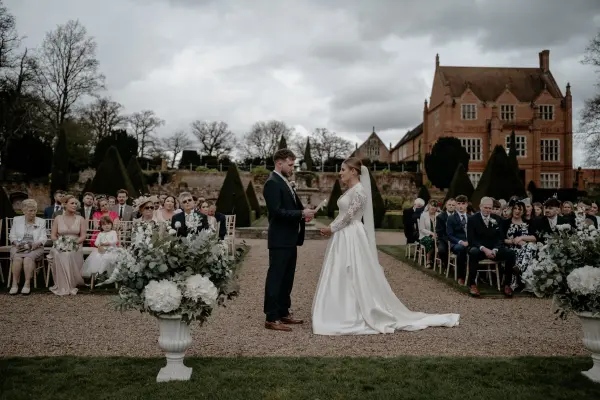 A charming outdoor ceremony setting with a couple exchanging vows, surrounded by lush gardens and elegant floral arrangements.