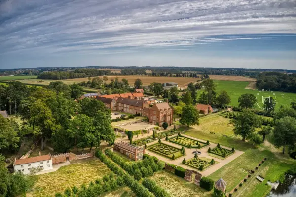 Aerial view of a picturesque wedding venue featuring manicured gardens, rustic buildings, and expansive green fields under a vibrant sky.