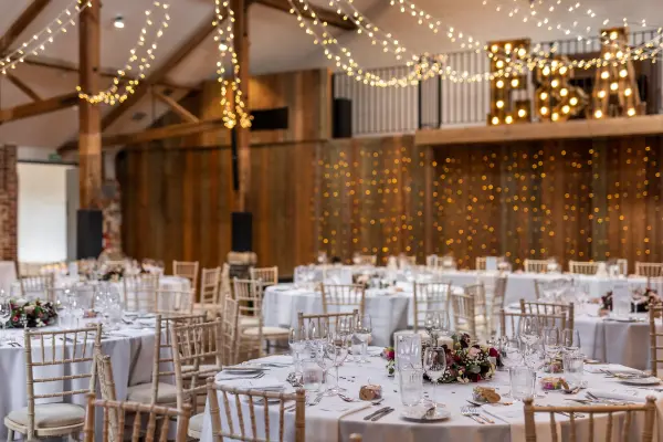 Charming reception space featuring elegant round tables adorned with floral centerpieces, warm wood accents, and enchanting string lights.
