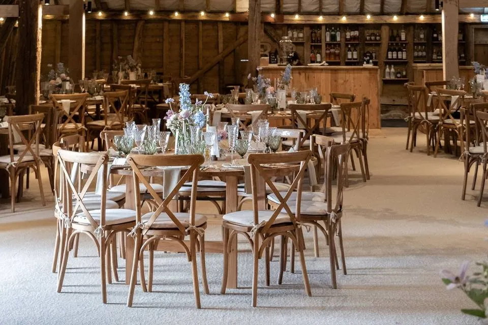 Rustic barn reception space featuring wooden tables adorned with floral centerpieces and a cozy bar setup in the background.
