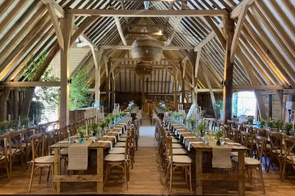 Rustic barn interior featuring elegant wooden beams, long reception tables adorned with greenery, and a warm, inviting atmosphere.