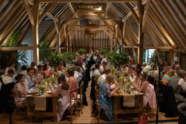 Elegant rustic barn reception with beautifully set long tables, lush greenery, and guests enjoying the festive atmosphere.