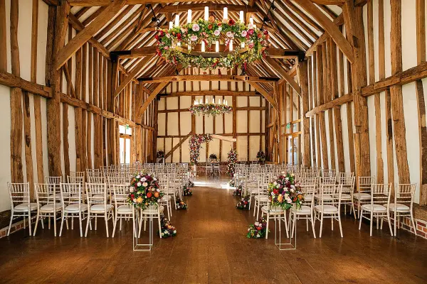 Rustic barn interior with exposed wooden beams, elegantly arranged chairs, and floral accents creating a charming ceremony space.