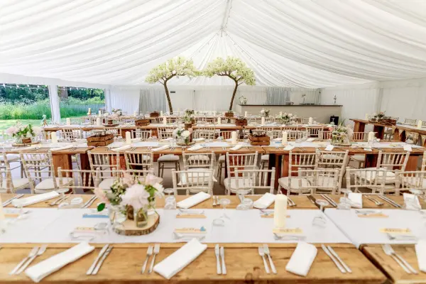Elegant marquee with rustic wooden tables, chiavari chairs, and floral centerpieces, set up for a charming wedding reception.
