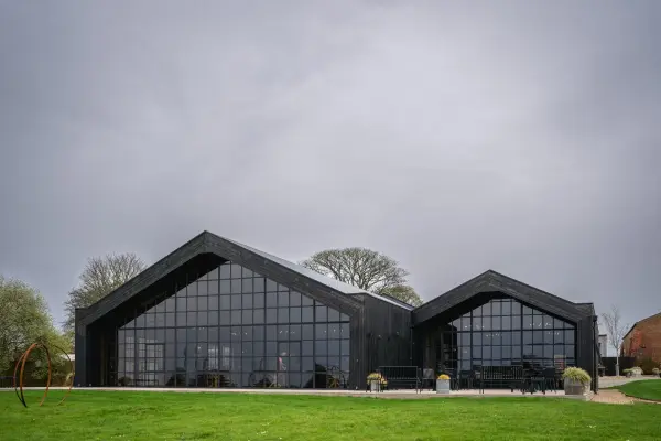 Stylish black barn venue featuring large windows, lush green lawn, and modern architecture, perfect for contemporary weddings.