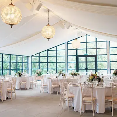 Bright, airy space features elegant tables with white linens, chic chairs, and large windows, perfect for a modern wedding reception.