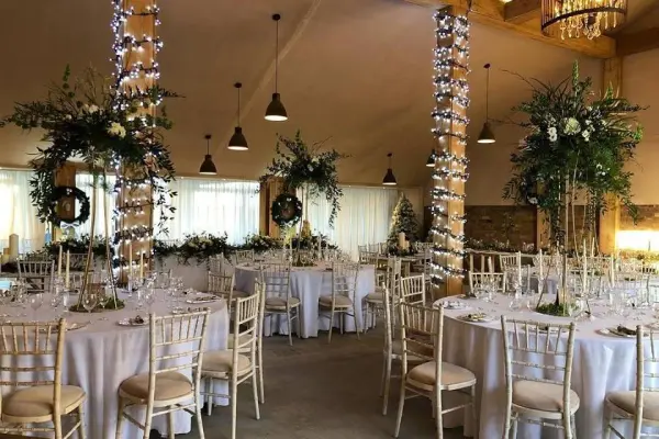 Elegant dining setup featuring round tables adorned with white linens, floral arrangements, and twinkling lights in a charming reception space.