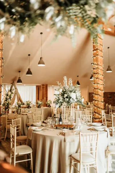Elegant reception area featuring round tables adorned with floral centerpieces, chairs, and soft lighting in a rustic setting.