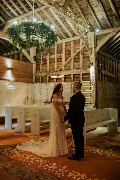 Intimate rustic barn interior featuring a wooden altar, elegant chandeliers, and romantic lighting for a memorable wedding ceremony.