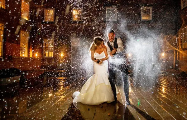 A couple joyfully celebrates under a sparkling spray at night, surrounded by warm lights and a charming venue backdrop.
